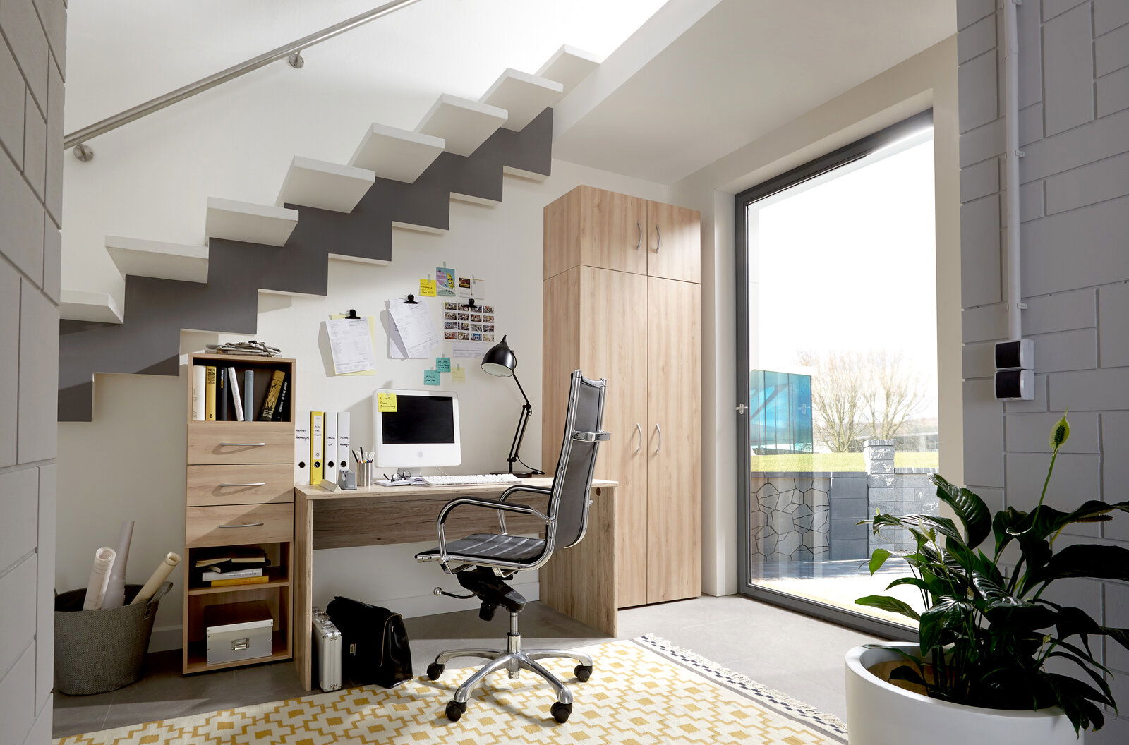 Moderner Arbeitsplatz unter einer Treppe mit Schreibtisch, Drehstuhl und Holzschränken, seitliche Perspektive.