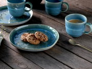 Blau-grün glasiertes Keramikgeschirr-Set mit Teller und Tassen auf rustikalem Holztisch, Teller mit Cookies, seitliche Perspektive
