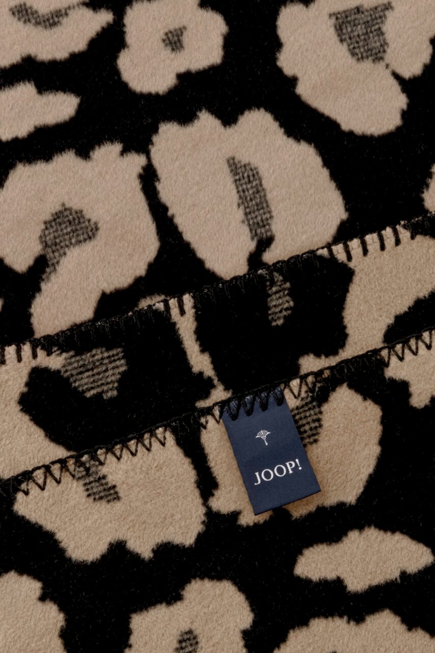 Nahaufnahme einer JOOP! Wohndecke mit Leopardenmuster in Beige und Schwarz, Etikett sichtbar.