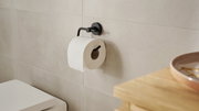 Schwarzer Toilettenpapierhalter der Serie tesa MOON BLACK, montiert an einer Badezimmerwand mit einer Rolle Toilettenpapier, seitliche Perspektive.