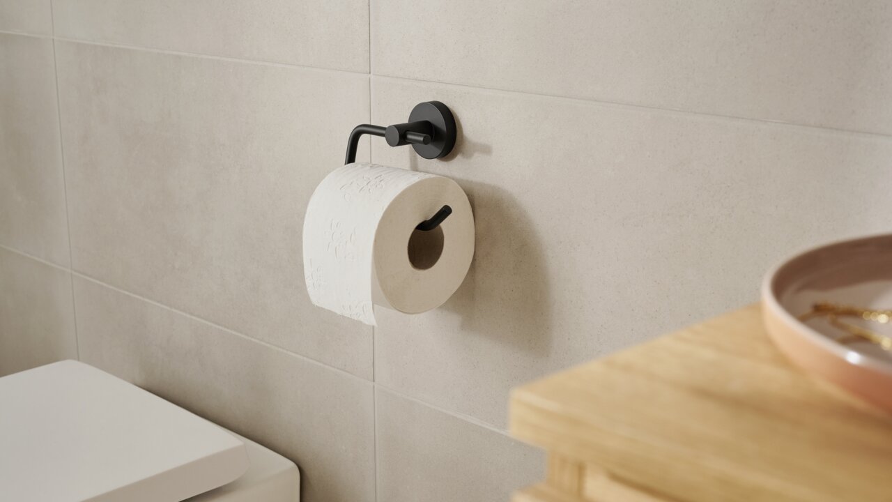 Schwarzer Toilettenpapierhalter der Serie tesa MOON BLACK, montiert an einer Badezimmerwand mit einer Rolle Toilettenpapier, seitliche Perspektive.
