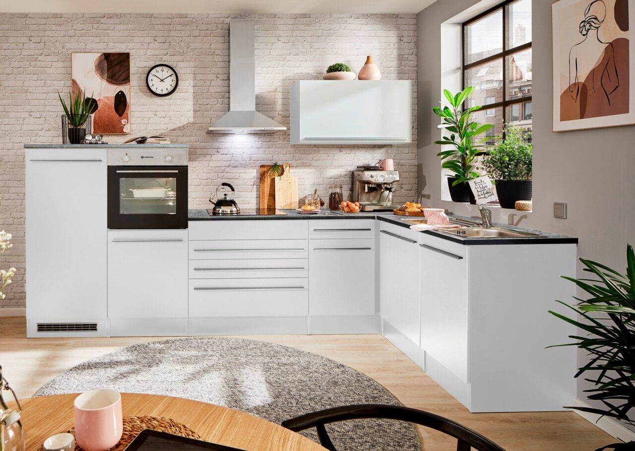 Moderne weiße Küche mit Eckunterschrank, Backofen, Herd und Spüle, aus der Perspektive eines Esszimmers mit Blick auf die Arbeitsfläche und Fenster.
