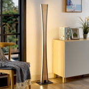 Schlanke LED-Stehlampe in Holzoptik mit schwarzem Rahmen und warmweißem indirektem Licht, freistehend auf quadratischem Sockel neben Sideboard im Wohnzimmer, frontale Perspektive.