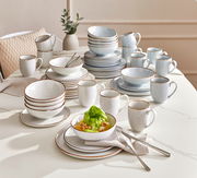 Kombiservice Bergen 24-tlg, bestehend aus Tellern, Schalen und Tassen in einem eleganten Design mit braunem Rand, auf einem Tisch arrangiert. Perspektive von schräg oben.