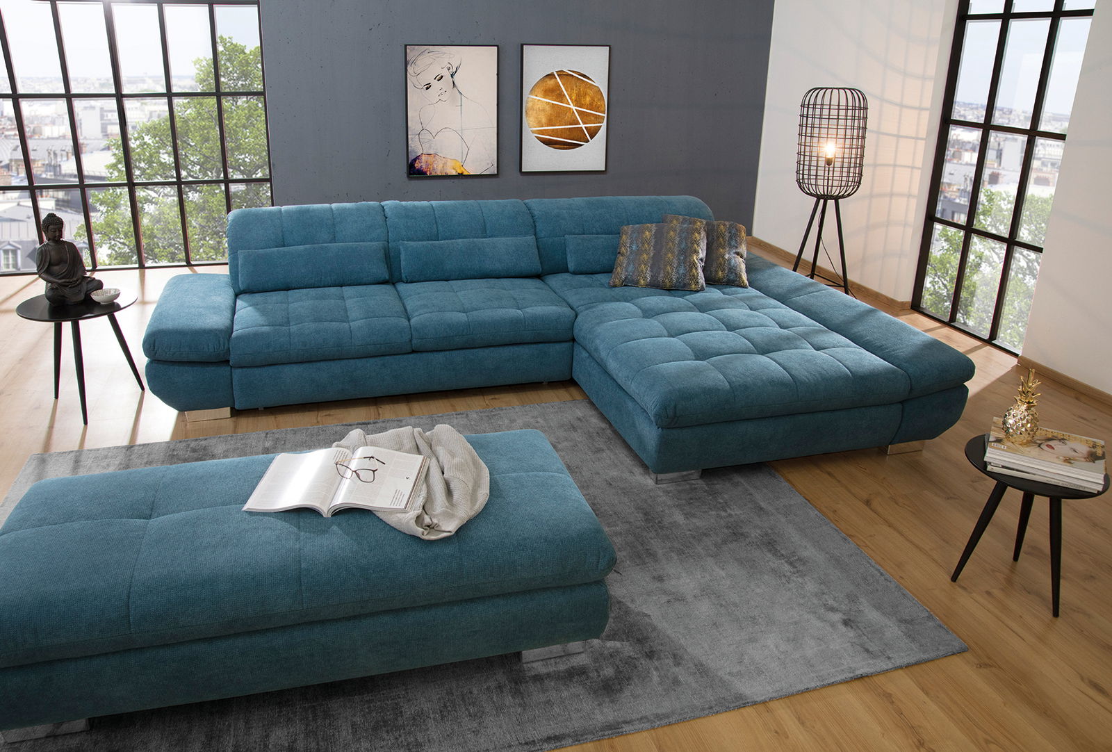 Zurbrüggen Hocker PRIDE Moderne Wohnlandschaft in U-Form mit Longchair in blauer Stoffausführung, abgebildet aus einer leicht erhöhten Perspektive in einem hellen Wohnzimmer mit großen Fenstern.