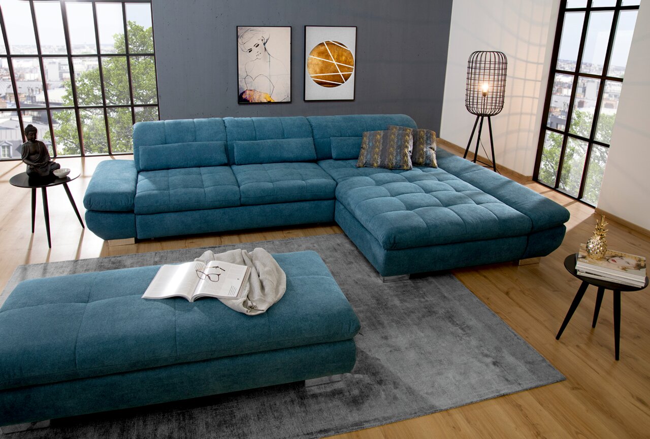 Moderne Wohnlandschaft in U-Form mit Longchair in blauer Stoffausführung, abgebildet aus einer leicht erhöhten Perspektive in einem hellen Wohnzimmer mit großen Fenstern.