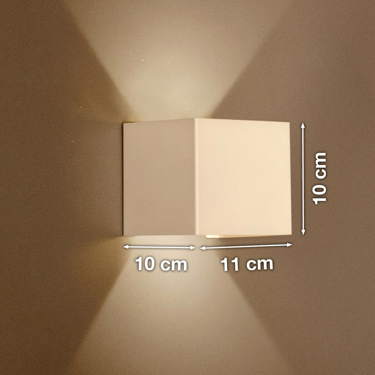 Weiße, kubische Wandleuchte mit Up-&-Downlight an beiger Wand, Lichtkegel nach oben und unten, Maße ca. 10 cm hoch, 10 cm tief und 11 cm breit, Frontansicht leicht seitlich.