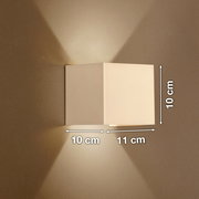 Weiße, kubische Wandleuchte mit Up-&-Downlight an beiger Wand, Lichtkegel nach oben und unten, Maße ca. 10 cm hoch, 10 cm tief und 11 cm breit, Frontansicht leicht seitlich.
