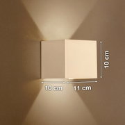 Weiße, kubische Wandleuchte mit Up-&-Downlight an beiger Wand, Lichtkegel nach oben und unten, Maße ca. 10 cm hoch, 10 cm tief und 11 cm breit, Frontansicht leicht seitlich.