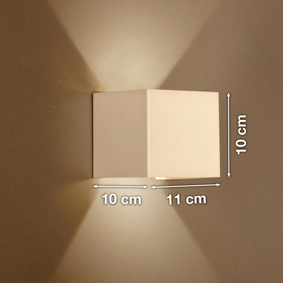 Weiße, kubische Wandleuchte mit Up-&-Downlight an beiger Wand, Lichtkegel nach oben und unten, Maße ca. 10 cm hoch, 10 cm tief und 11 cm breit, Frontansicht leicht seitlich.