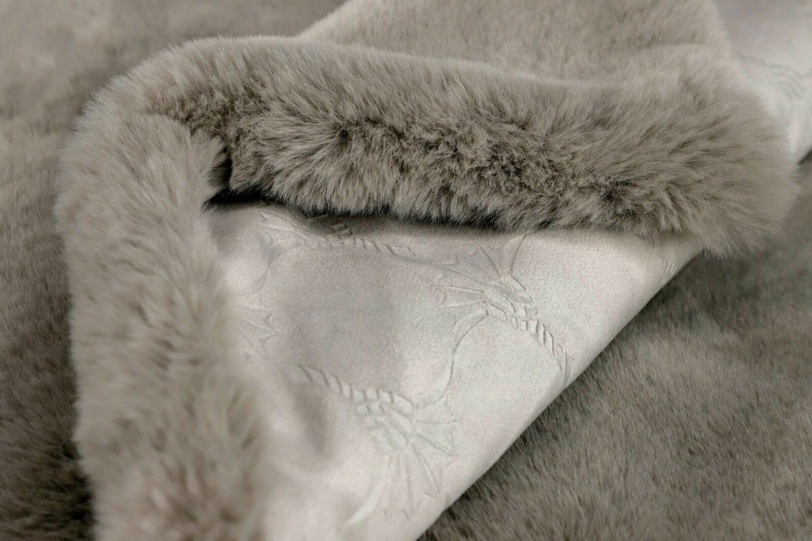 Nahaufnahme einer grauen Wohndecke mit weichem, flauschigem Rand und dezentem Muster, Perspektive von oben.