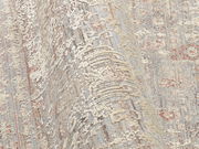 Nahaufnahme eines Designer-Teppichs mit detailliertem Muster in Beige- und Grautönen, aus seitlicher Perspektive aufgenommen.