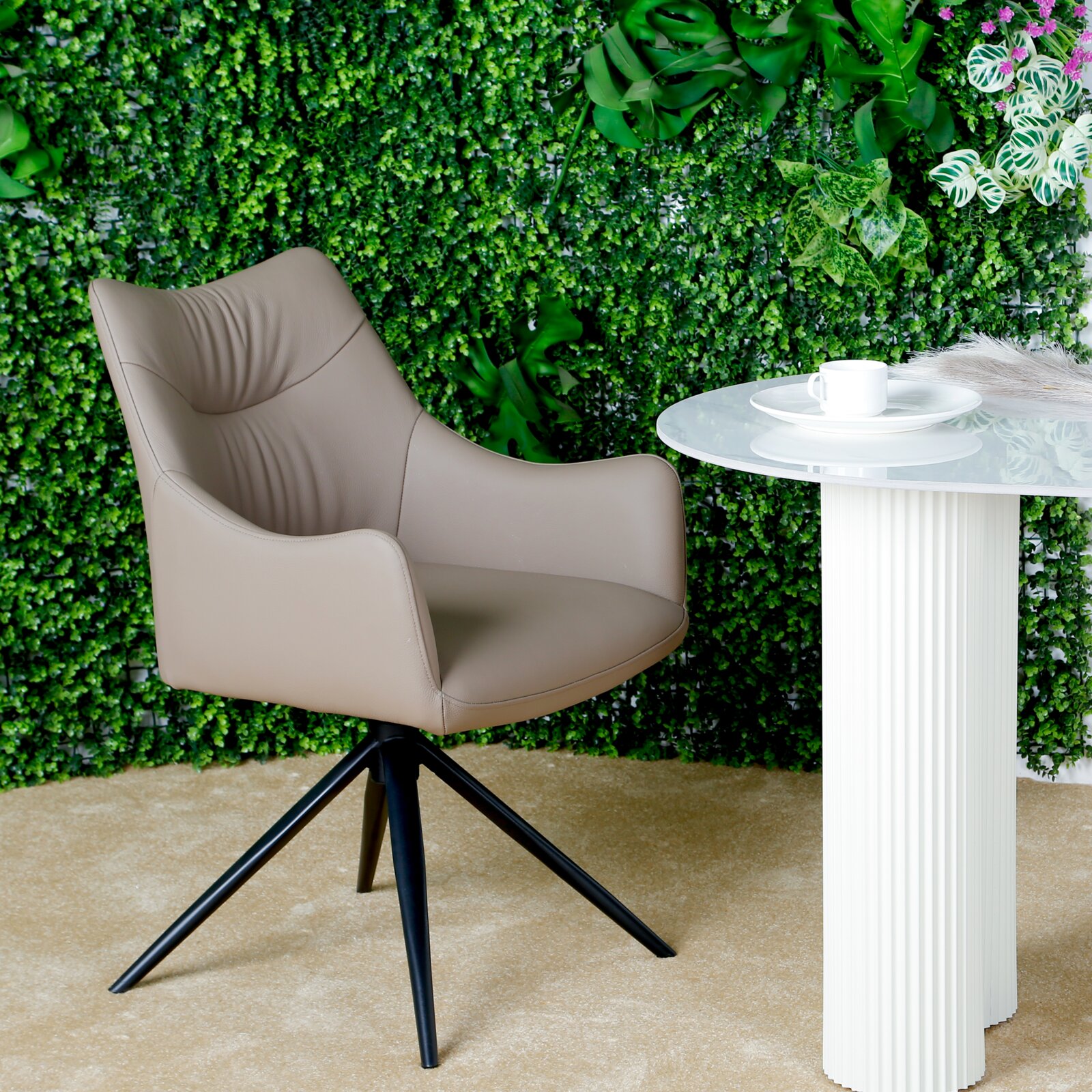 Novel Fauteuil BELFORT Moderne fauteuil in bruin met een zwart metalen frame, gezien vanaf de zijkant, tegen een groene achtergrond en naast een witte tafel.