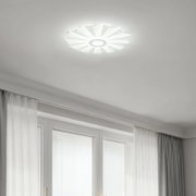 Moderne weiße LED-Deckenleuchte in Blumenform mit radialen Lamellen, eingeschaltet an der Zimmerdecke über Fenstern und Vorhängen, Aufnahme aus Untersicht nach oben