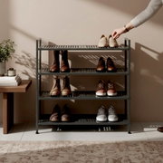 Modernes graues Schuhregal aus Metall mit vier Ebenen, bestückt mit verschiedenen Schuhpaaren; Hand legt ein Paar oben ab, frontal aus leicht erhöhter Perspektive im Wohnraum.