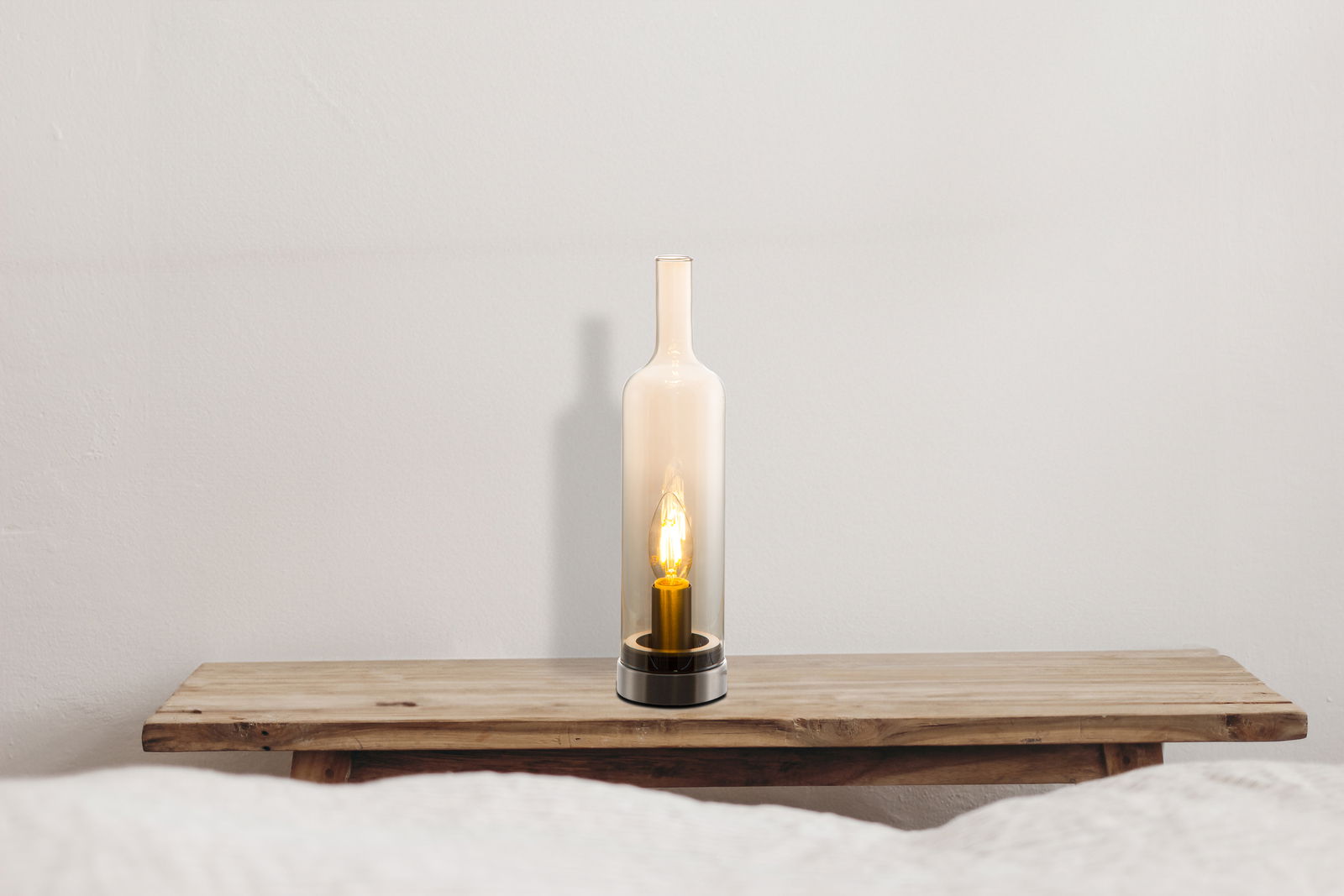 Moderne Tischleuchte in Flaschenform mit warmem Licht, frontal auf einem Holztisch platziert.