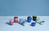 Verschiedene bunte Fruchtbehälter in elliptischer Form, gefüllt mit Obst und Nüssen, auf einer blauen Oberfläche aus der Vogelperspektive.