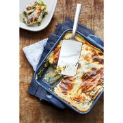 Lasagneheber aus Edelstahl in einer blauen Auflaufform mit Lasagne, von oben fotografiert.
