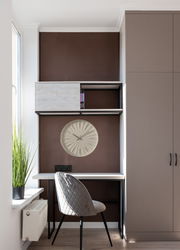 Moderne Wanduhr in einem stilvollen Arbeitsbereich, frontal betrachtet. Die Uhr hat ein minimalistisches Design und ist in einem Regal über einem Schreibtisch platziert.