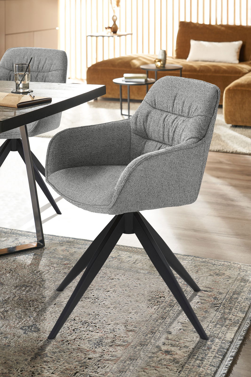 Grauer Armlehnstuhl mit schwarzem Metallgestell, seitliche Perspektive, in modernem Wohnzimmerambiente.