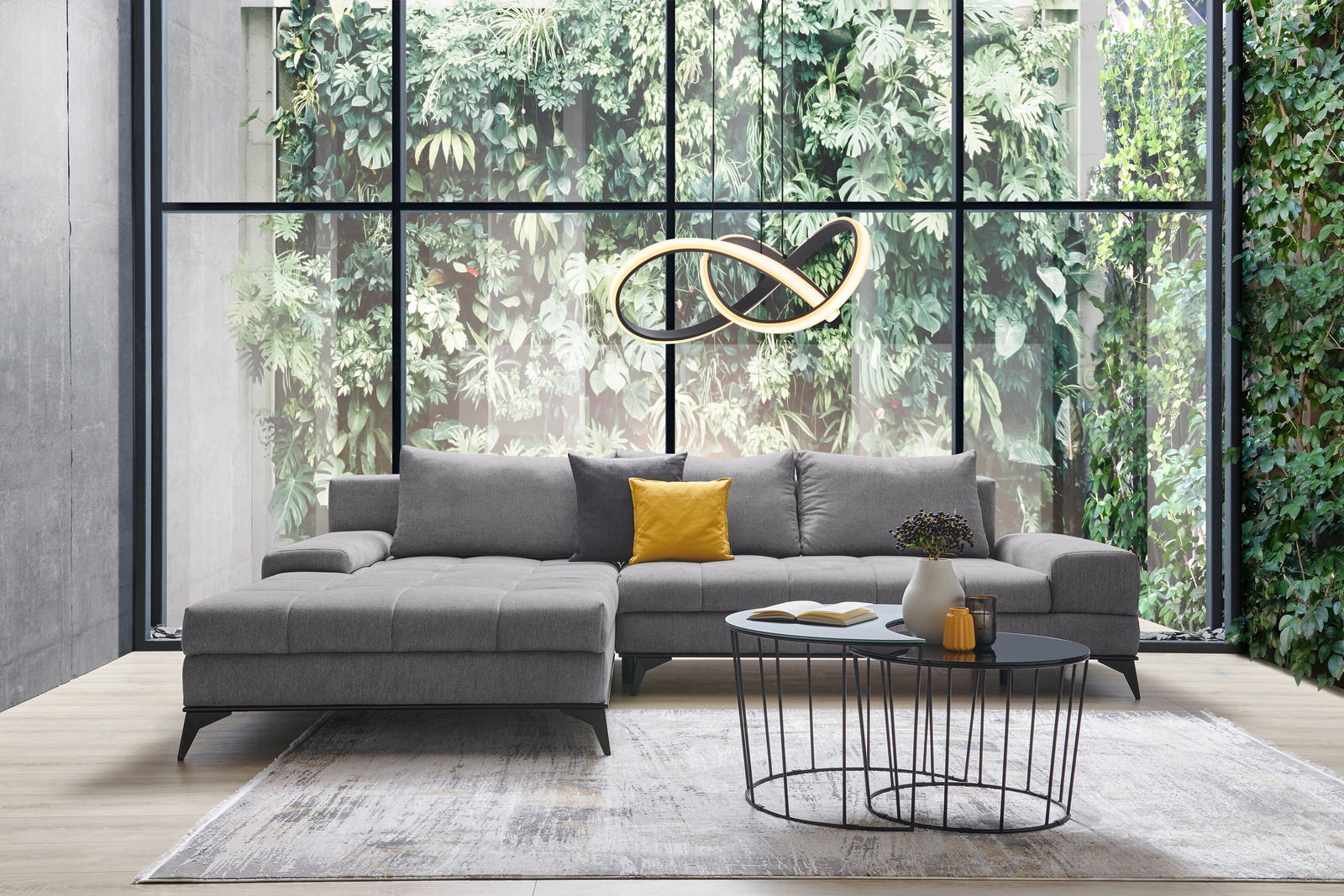 Graue Rundecke Ottli in modernem Wohnzimmer mit großen Fenstern und grüner Pflanzenwand, Vorderansicht