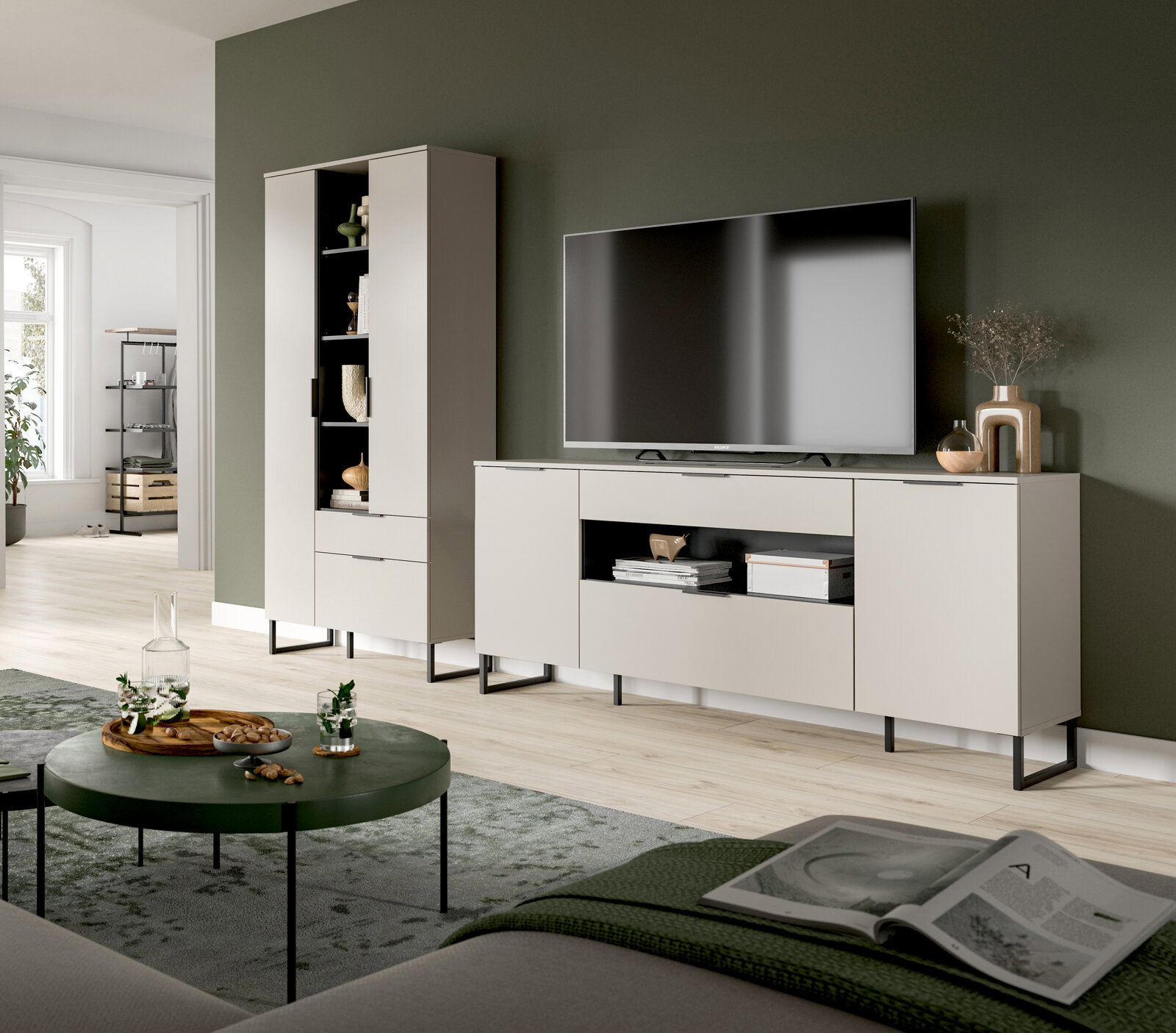 Modernes Wohnzimmer mit hellgrauem TV-Lowboard und passendem Hochschrank auf schwarzen Metallfüßen vor dunkelgrüner Wand, TV und Deko darauf; Perspektive: frontale Ansicht mit leichtem Weitwinkel aus Sitzhöhe.