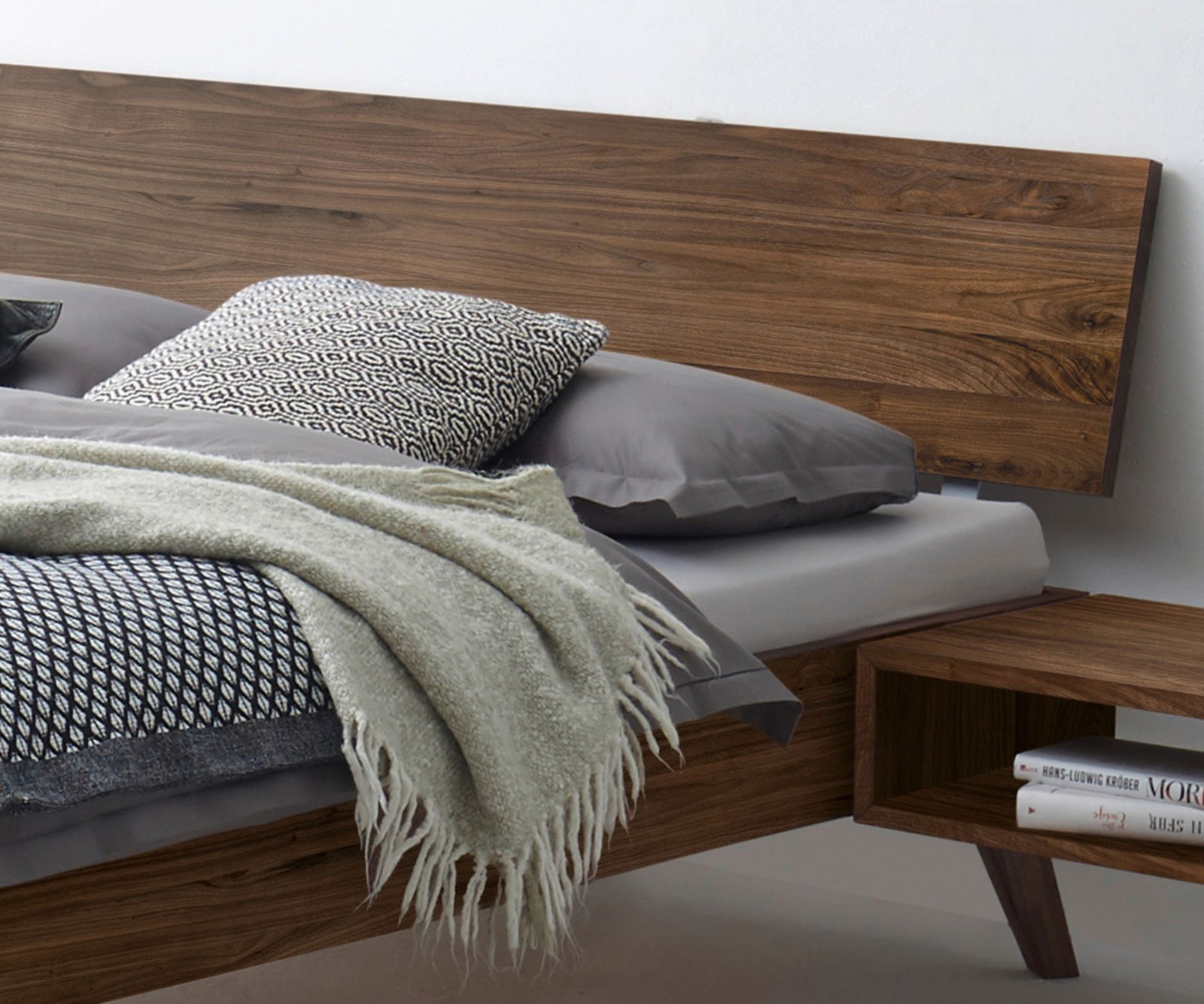 Modernes Bettgestell aus Holz mit Kopfteil, seitliche Perspektive, dekoriert mit Kissen und Decke.