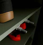 Nahaufnahme eines Schuhschranks mit einem schwarzen Stiefel und roten Schuhen auf den Regalen, seitliche Perspektive