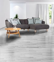 Grijze hoekbank met lichtblauwe kussens en een ronde houten salontafel in een moderne woonkamer, gezien vanaf de zijkant.