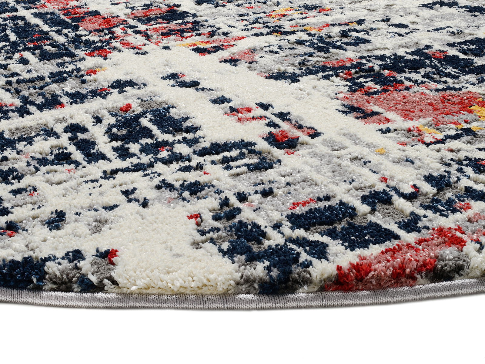 Nahaufnahme eines Designer-Teppichs mit abstraktem Muster in Blau, Rot, Grau und Weiß, perspektivisch von der Seite aufgenommen.