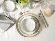 Draufsicht auf eine elegant gedeckte Festtafel mit cremefarbenem Geschirr in Craquelé-Optik, Besteck, Gläsern, grauer Stoffserviette und weißen Blüten