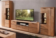 Wohnwand aus massivem Holz im Wohnzimmer: TV-Lowboard mit Schubladen und offenem Fach, flankiert von zwei hohen Vitrinenschränken mit Glasböden und Beleuchtung, frontale Perspektive