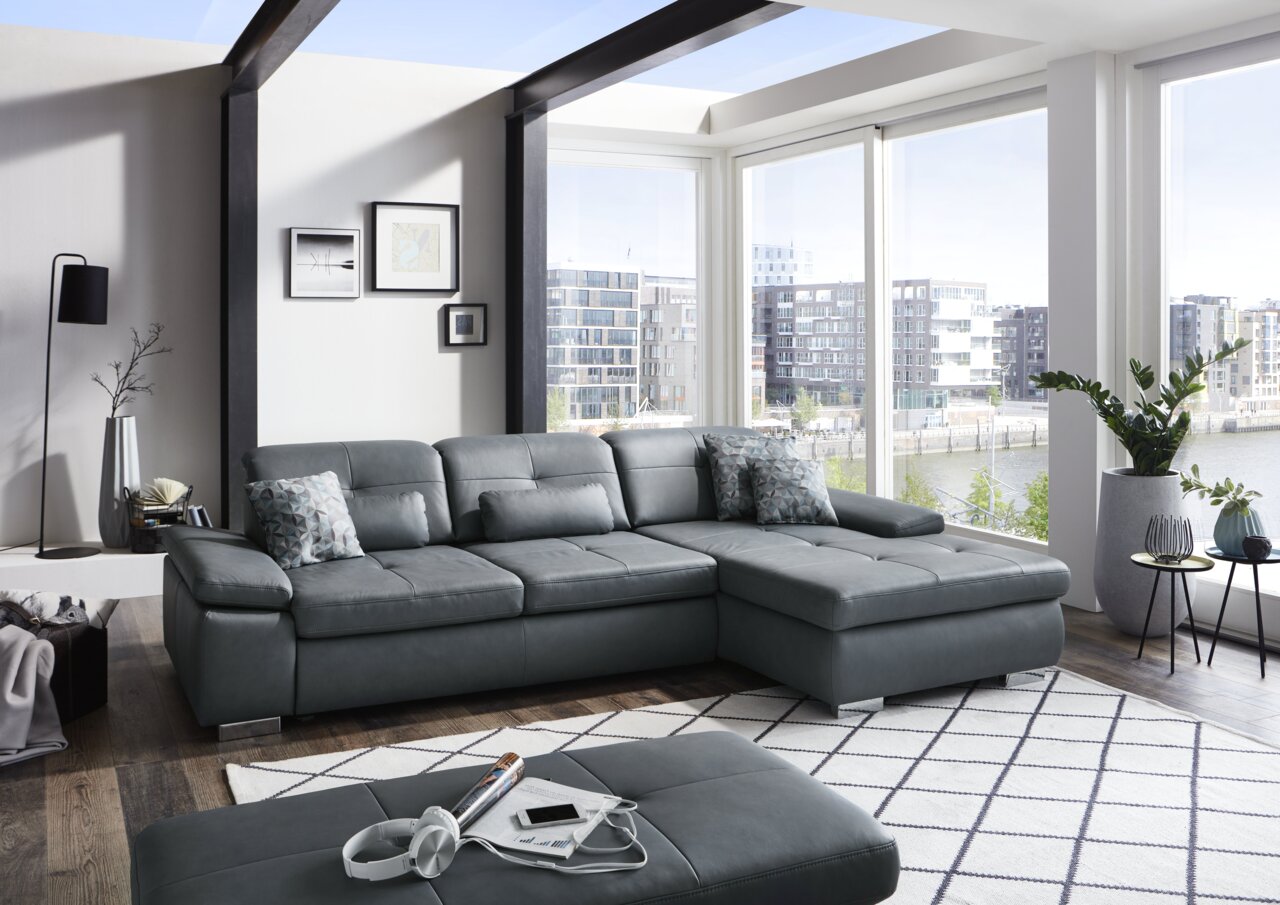 Moderne Longchairkombination in einem hellen Wohnzimmer mit großen Fenstern und Blick auf die Stadt. Perspektive von vorne links.