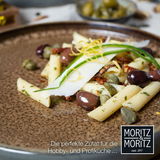 Nahaufnahme eines stilvoll angerichteten Tellers mit Penne, Oliven, Kapern und Zucchinistreifen auf einem beige-braunen Tafelservice.