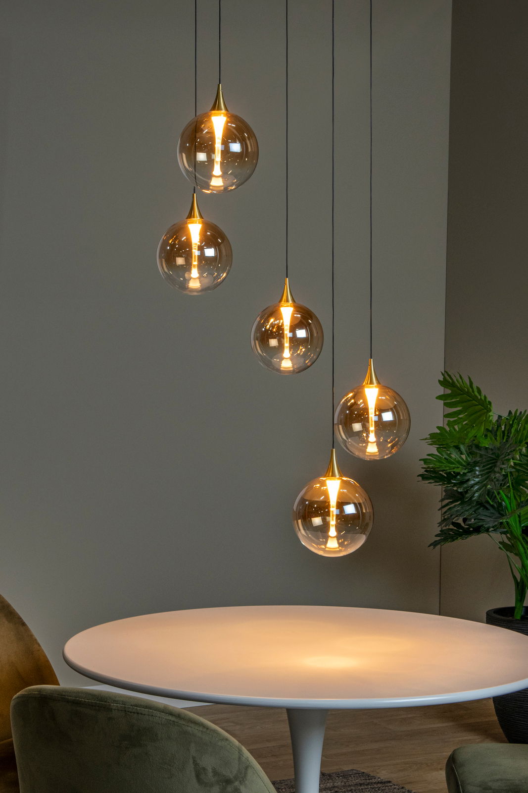 Moderne Hängeleuchte mit fünf kugelförmigen, goldenen Lampenschirmen, die in unterschiedlichen Höhen über einem runden Tisch hängen. Seitliche Perspektive.