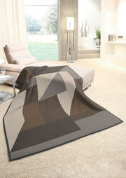 Moderne Wohndecke 150x200cm in geometrischem Design, drapiert auf einem Sofa in einem hellen Wohnzimmer mit Blick auf den Garten.