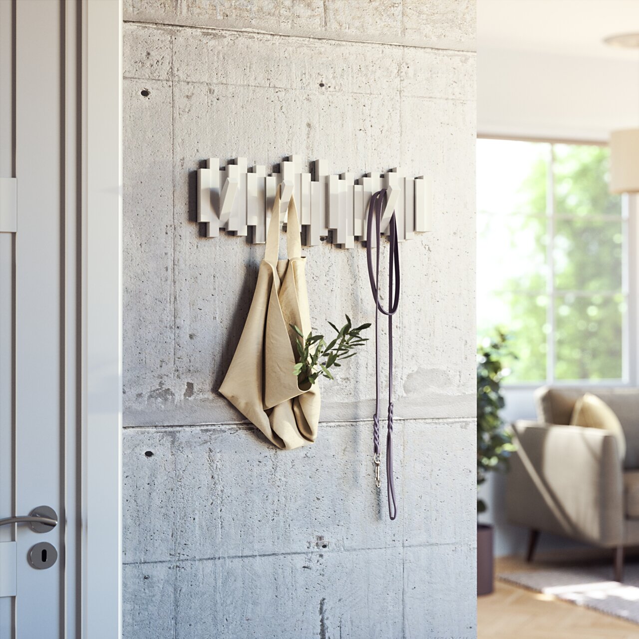 Moderne Wandgarderobe aus Metall mit Haken, an der eine Tasche und ein Hundeleine hängen, in einem hellen Wohnzimmer mit Betonwand, seitliche Perspektive.