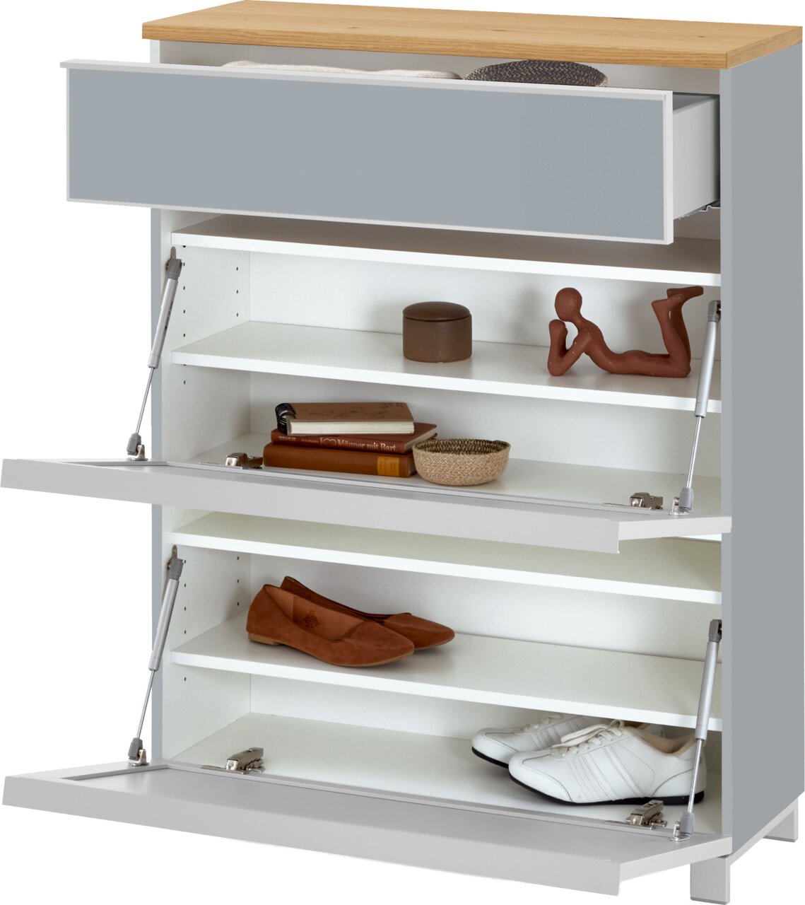 Moderner Schuhschrank in Weiß mit Holzoptik-Deckplatte und grauer Schubladenfront, mit geöffneter Schublade und zwei Klappfächern samt Einlegeböden, befüllt mit Schuhen und Deko, in schräger Frontansicht von leicht oben.
