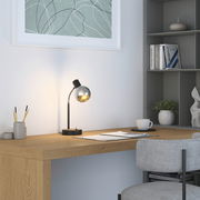 Moderne Tischleuchte mit gebogenem Hals und kugelförmigem Lampenschirm auf einem Schreibtisch, seitliche Perspektive.