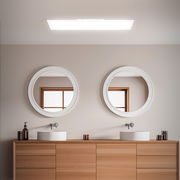 Rechteckige LED-Badleuchte in Weiß, an der Decke montiert, mit Blick auf ein modernes Badezimmer mit zwei runden Spiegeln und einem Holzwaschtisch.