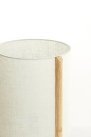Close-up van een tafellamp met een cilindervormige, lichte stoffen kap en een verticaal houten element aan de zijkant.