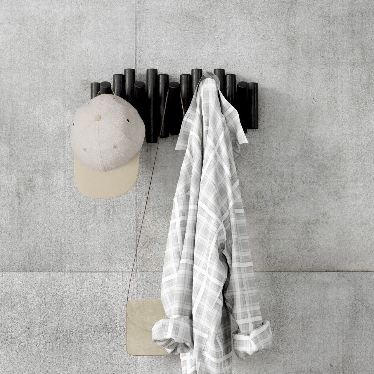 Moderne Wandgarderobe aus dunklem Holz mit Haken, an der eine beige Kappe, ein kariertes Hemd und eine kleine Tasche hängen, frontal an einer Betonwand montiert.
