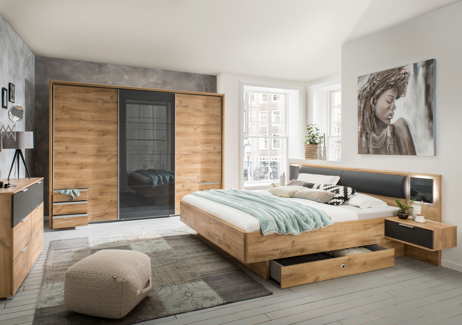 Modernes Schlafzimmer mit Schwebetürenschrank, Bettanlage und Kommode in Holzoptik, seitliche Perspektive.