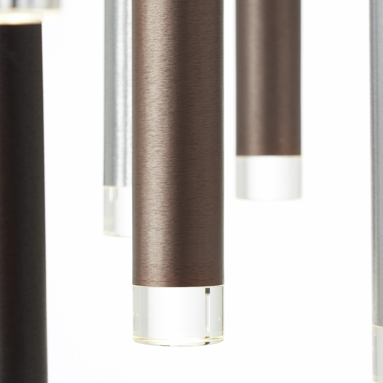 Nahaufnahme von hängenden, zylinderförmigen LED-Leuchten in verschiedenen Metalltönen mit klaren Endkappen, seitliche Perspektive
