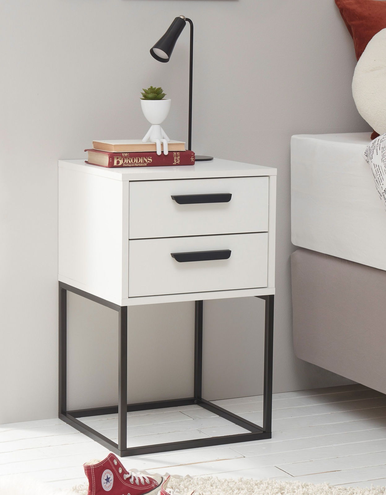Moderne weiße Nachtkommode mit zwei Schubladen und schwarzem Metallgestell, seitliche Perspektive.