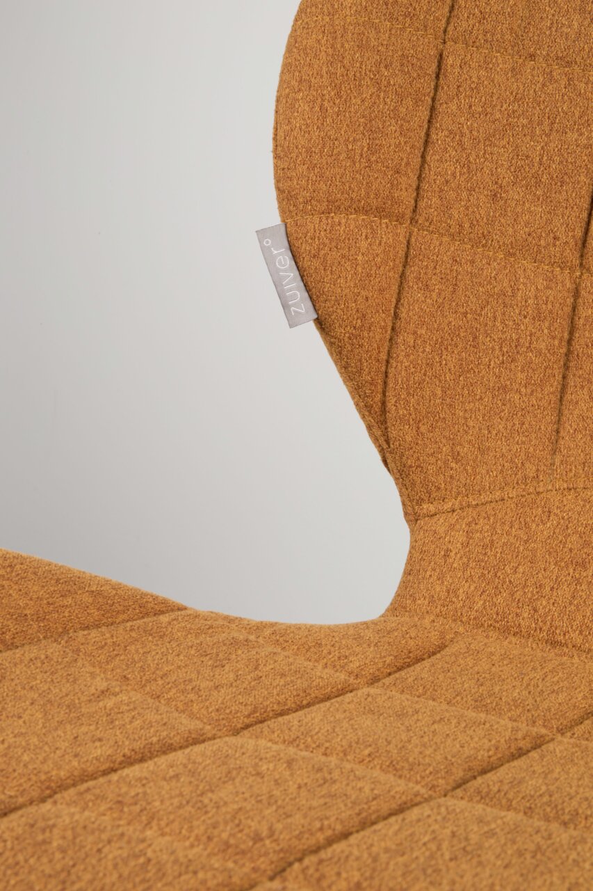 Nahaufnahme eines Stuhls mit orange-braunem Stoffbezug und sichtbarem Etikett, seitliche Perspektive