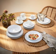 Elegantes Kombiservice Lido Black 30-teilig auf einem Holztisch, bestehend aus Tellern, Tassen und Schalen, mit einer modernen Tischdekoration aus Blumen und geflochtenen Platzsets, aus der Vogelperspektive fotografiert.