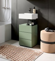 Modernes Badmöbel-Set: grüner Unterschrank mit drei Schubladen und weißem Aufsatzwaschbecken mit Chromarmatur, fotografiert in leichter Seitenansicht von vorn.