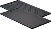 Zwei schwarze Grillplatten, eine mit glatter Oberfläche und eine mit geriffelter Oberfläche, in schräger Perspektive.
