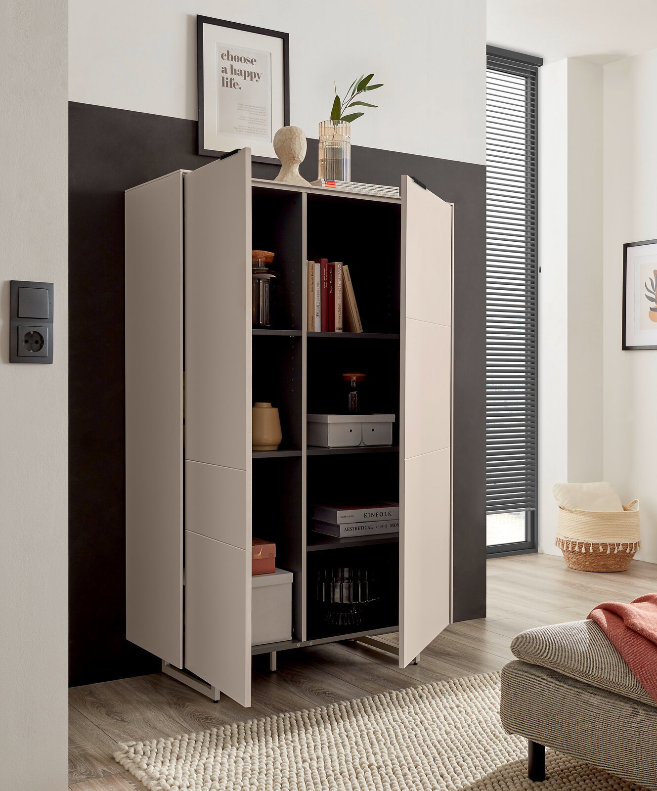 Modernes, hellgraues Highboard/Schrank mit zwei geöffneten Türen und schwarzen Innenfächern, dekoriert mit Büchern und Accessoires, in einem Wohnzimmer – Frontansicht in leichter Schrägperspektive von links.